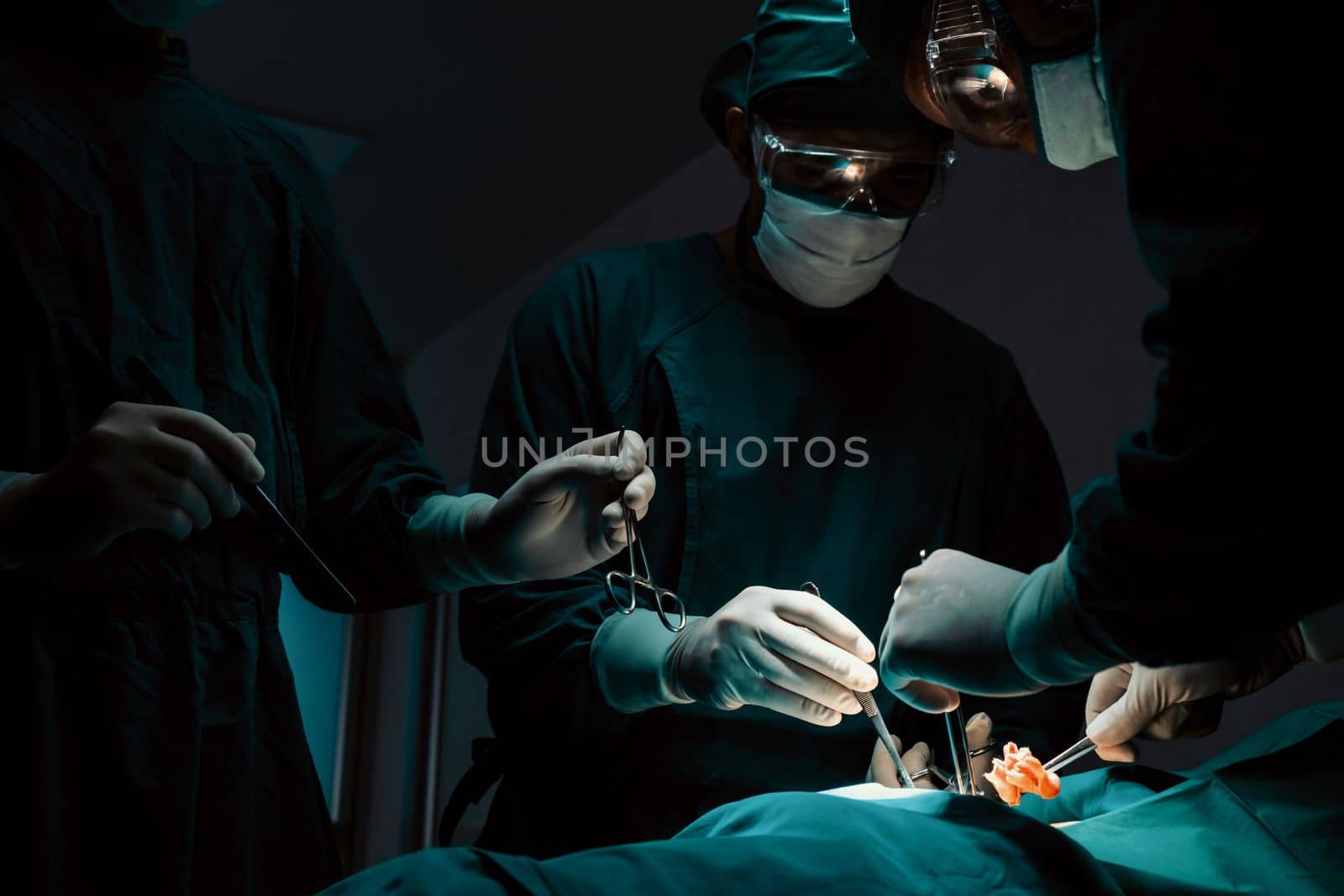 Surgical team performing surgery to patient in sterile operating room. In a surgery room lit by a lamp, a professional and confident surgical team provides medical care to an unconscious patient.