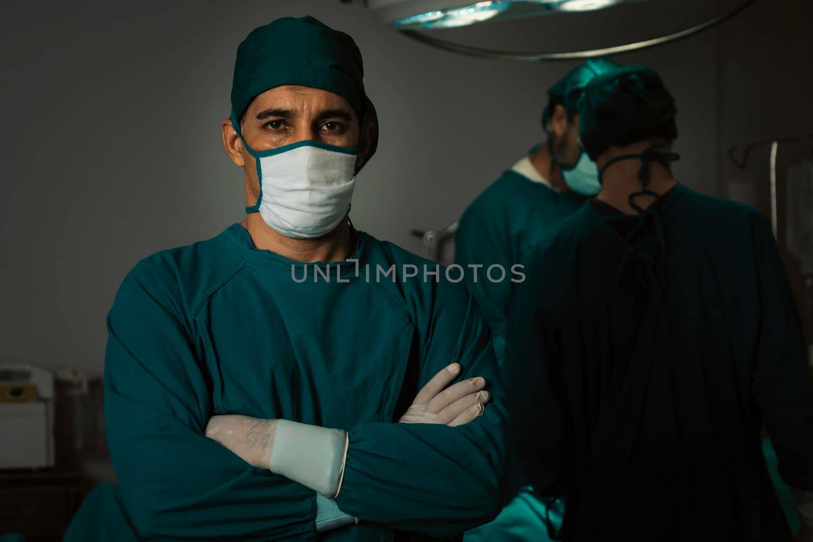 Portrait of surgical team leader in sterile operating room with his team and patient undergoing surgery. Confident and professional surgeon in full protective wear provide medical care to his patient.