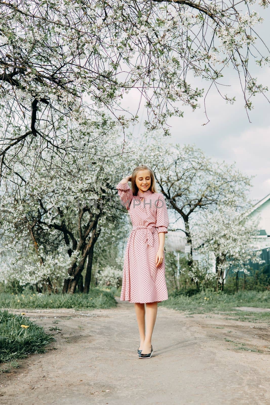 Blonde girl on a spring walk in the garden with cherry blossoms. Female portrait, close-up. A girl in a pink polka dot dress