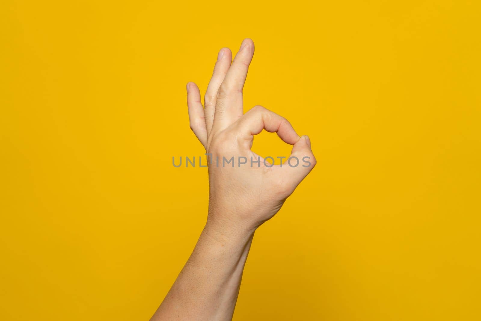 Strong hand of man making the ok gesture isolated on yellow background