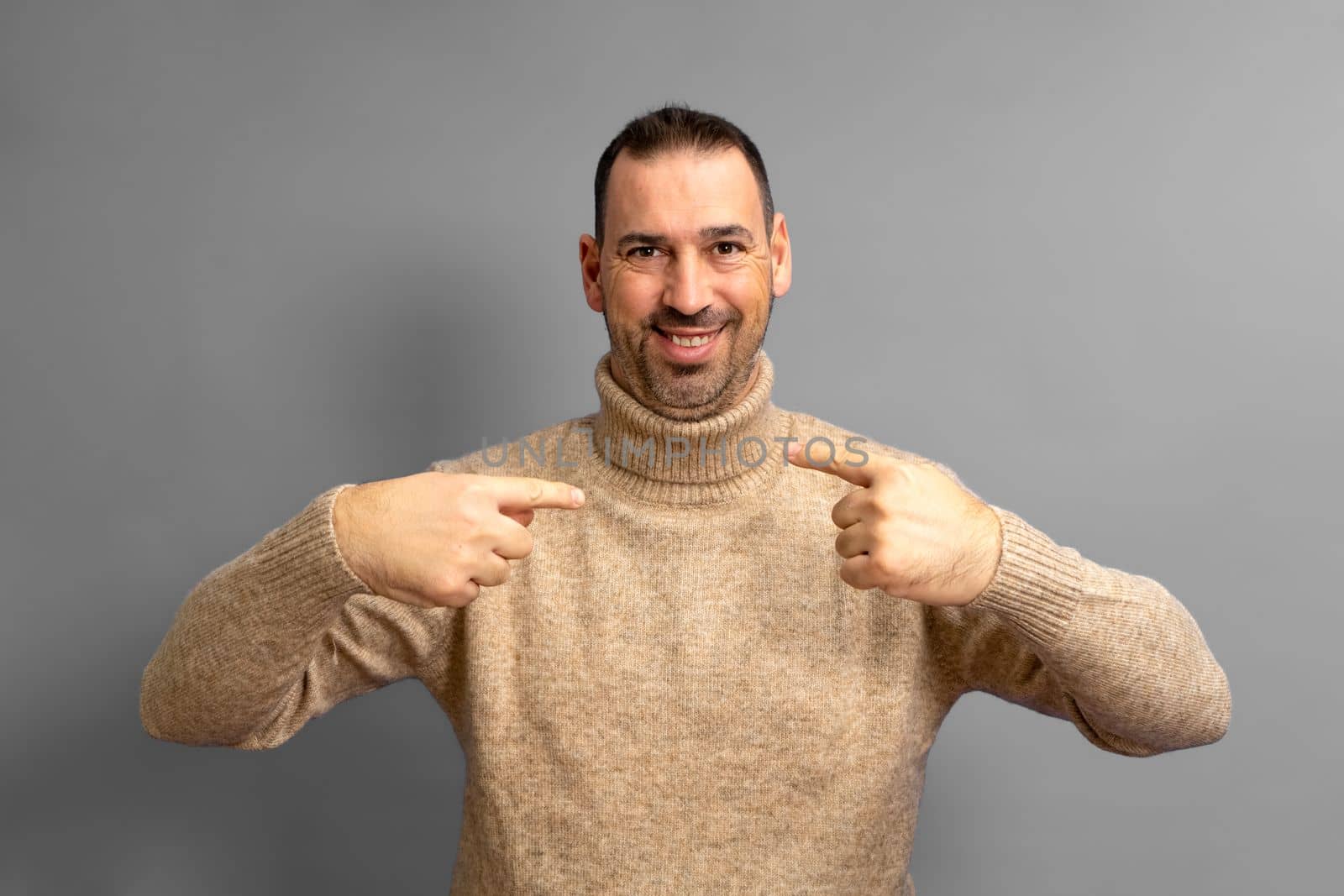 Handsome bearded hispanic man wearing turtleneck looking confident with smile on his face, pointing fingers to himself proud and happy.