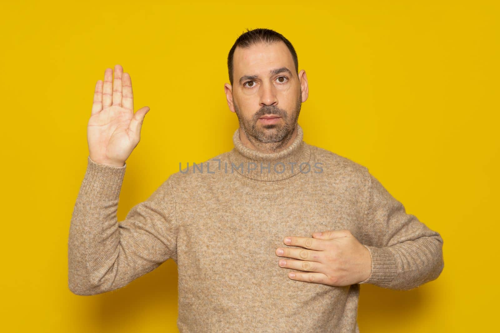 Bearded handsome man wearing turtleneck sweater standing over isolated yellow background. Swearing with hand on chest and open palm, swearing a pledge of allegiance