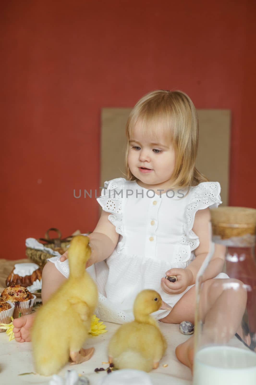 A little girl is sitting on the Easter table and playing with cute fluffy ducklings. The concept of celebrating happy Easter