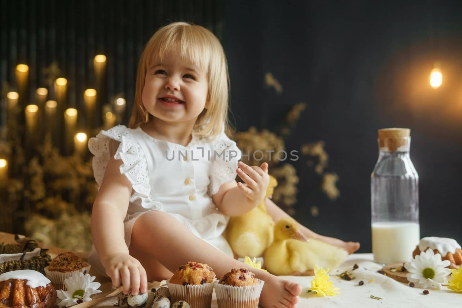 A little girl is sitting on the Easter table and playing with cute fluffy ducklings. The concept of celebrating happy Easter