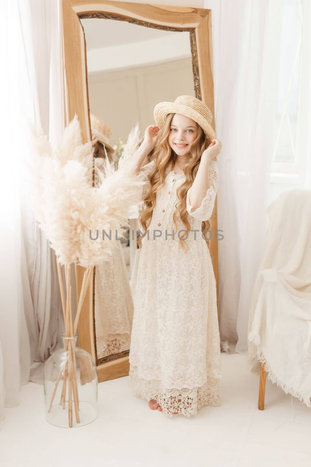 A beautiful teenage girl with long hair measures a straw hat in front of a mirror. Self-admiration of a blonde. selective focus