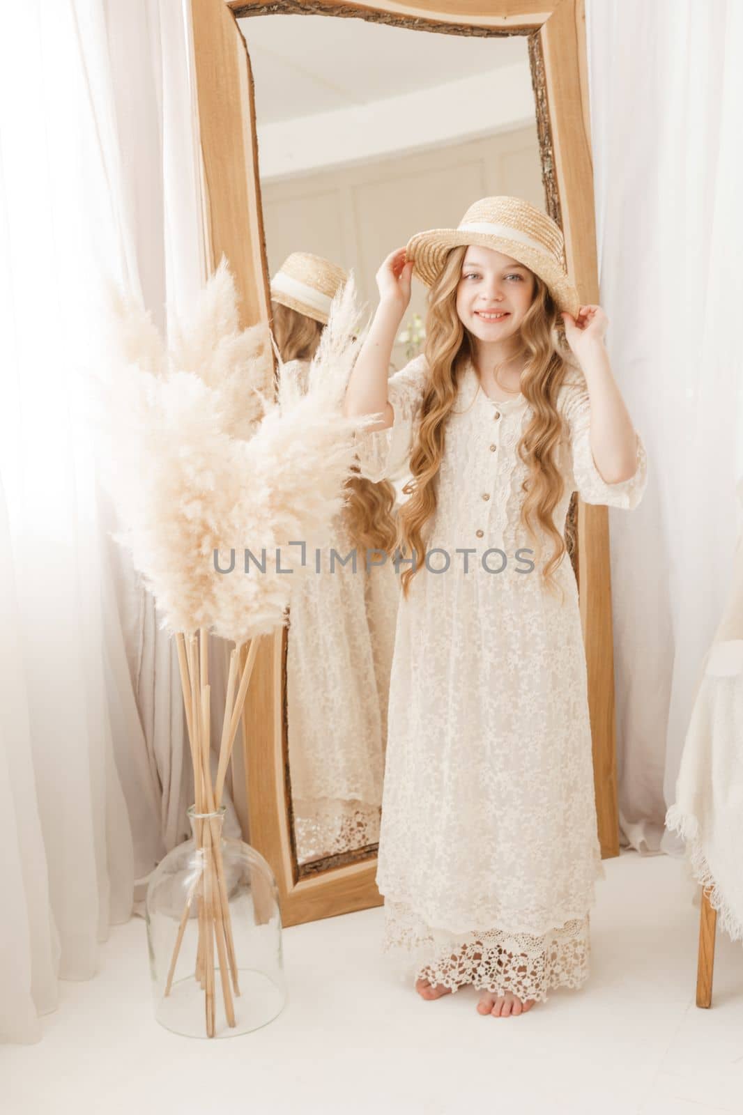 A beautiful teenage girl with long hair measures a straw hat in front of a mirror. Self-admiration of a blonde. selective focus