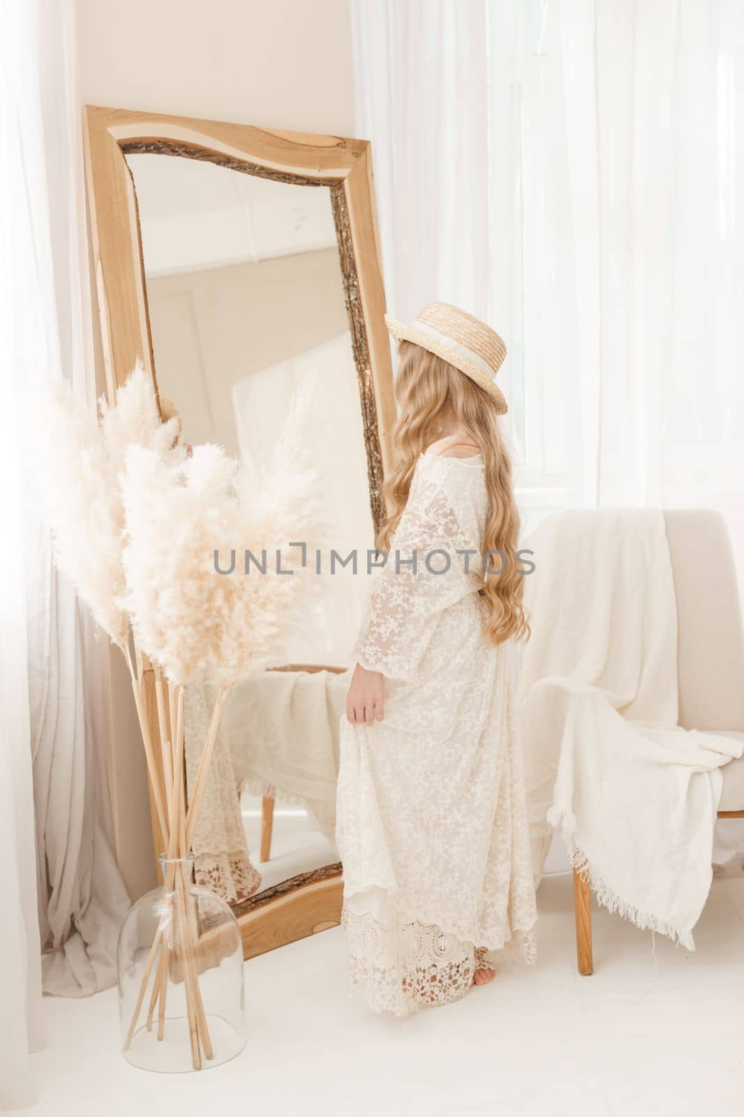 A beautiful teenage girl with long hair measures a straw hat in front of a mirror. Self-admiration of a blonde. selective focus
