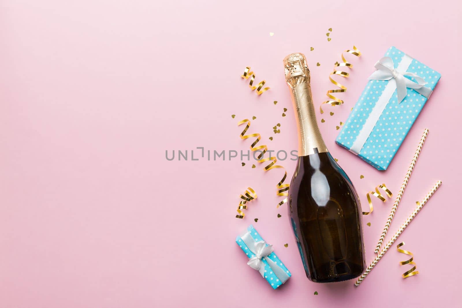 Bottle of champagne with colored glitter, confetti and gift box space for text on colorfull background, top view. Hilarious, christmas and birthday celebration.