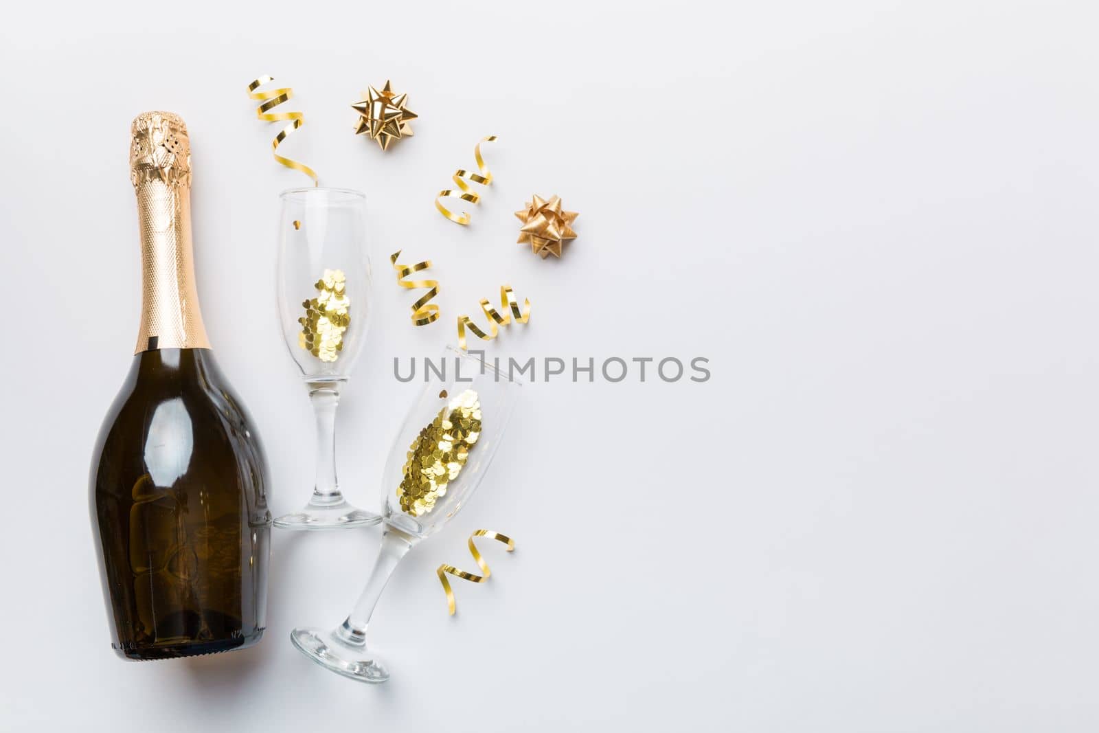 bottle of champagne with glasses and colorful confetti on colored background. top view flay lay.