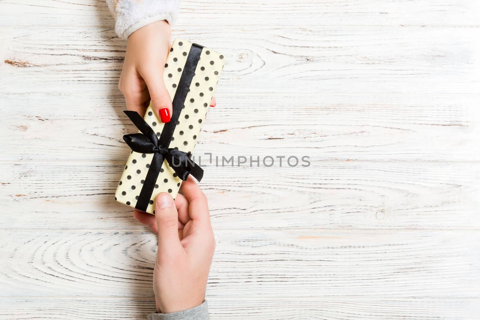 Top view of male and female hands holding present box on wooden background. Sharing a gift concept. Copy space.