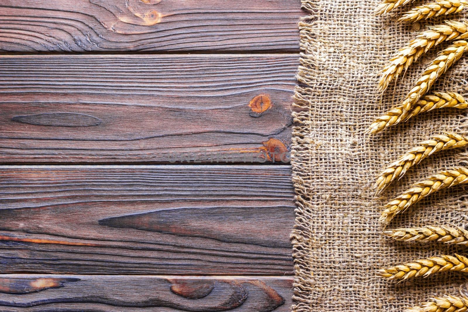 Wheat ears border on old burlap on wooden background.
