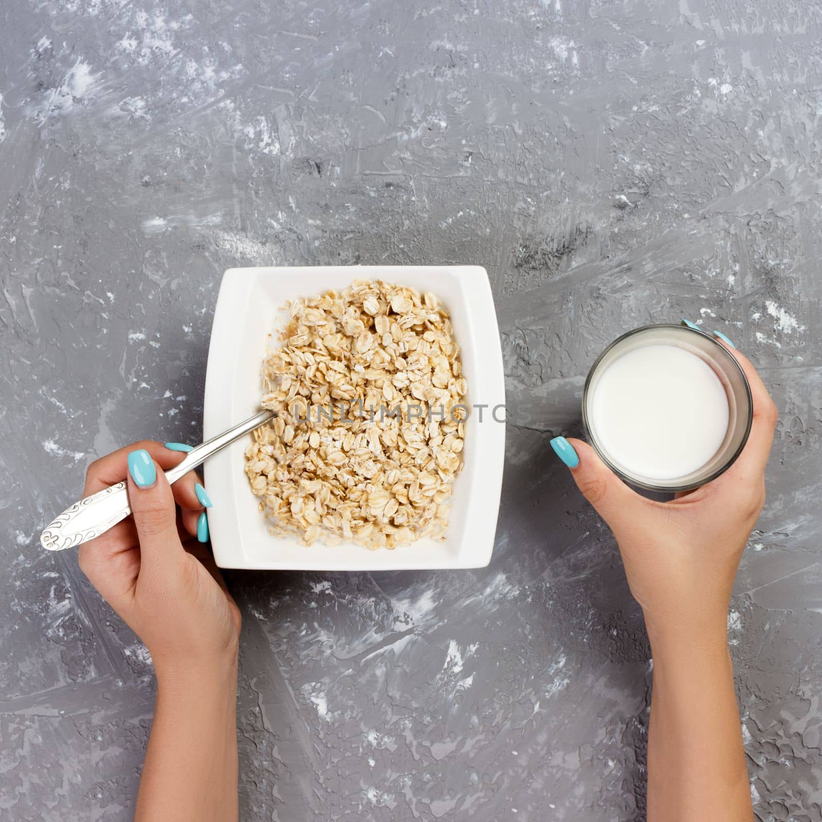 The girl took milk to pour it into oatmeal. Useful and healthy breakfast on a gray background, top view.