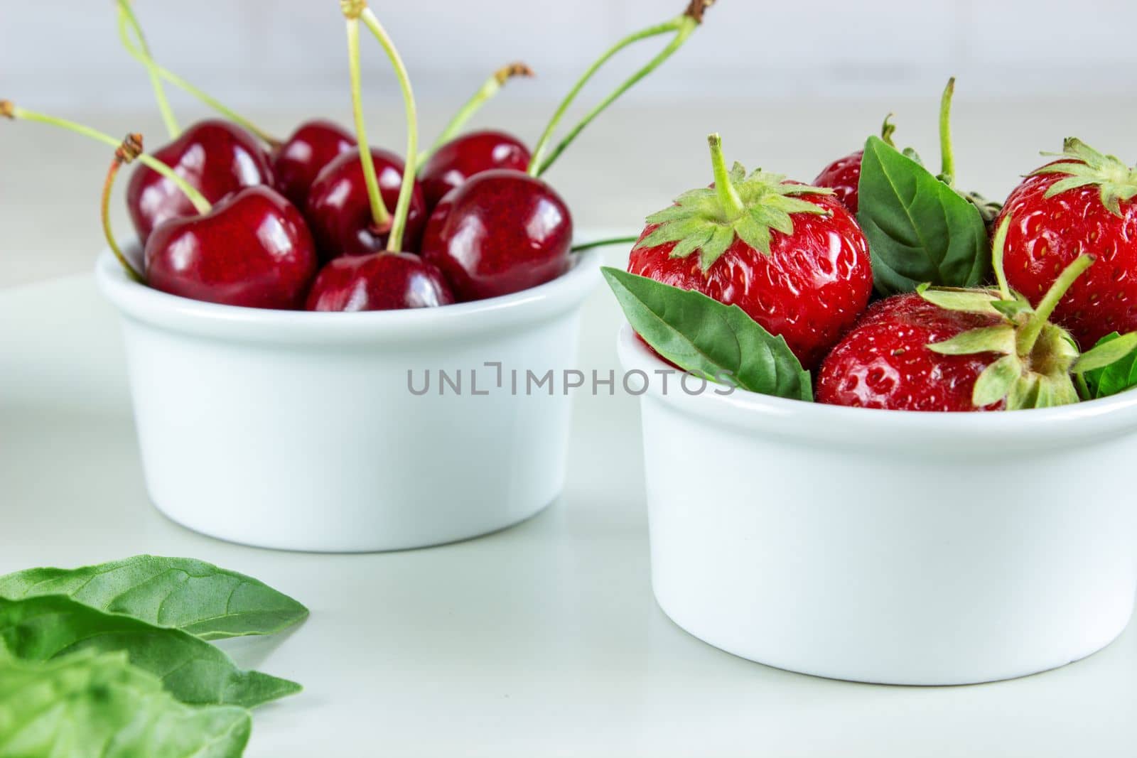 Ripe strawberries, mint and black cherry in bowls.