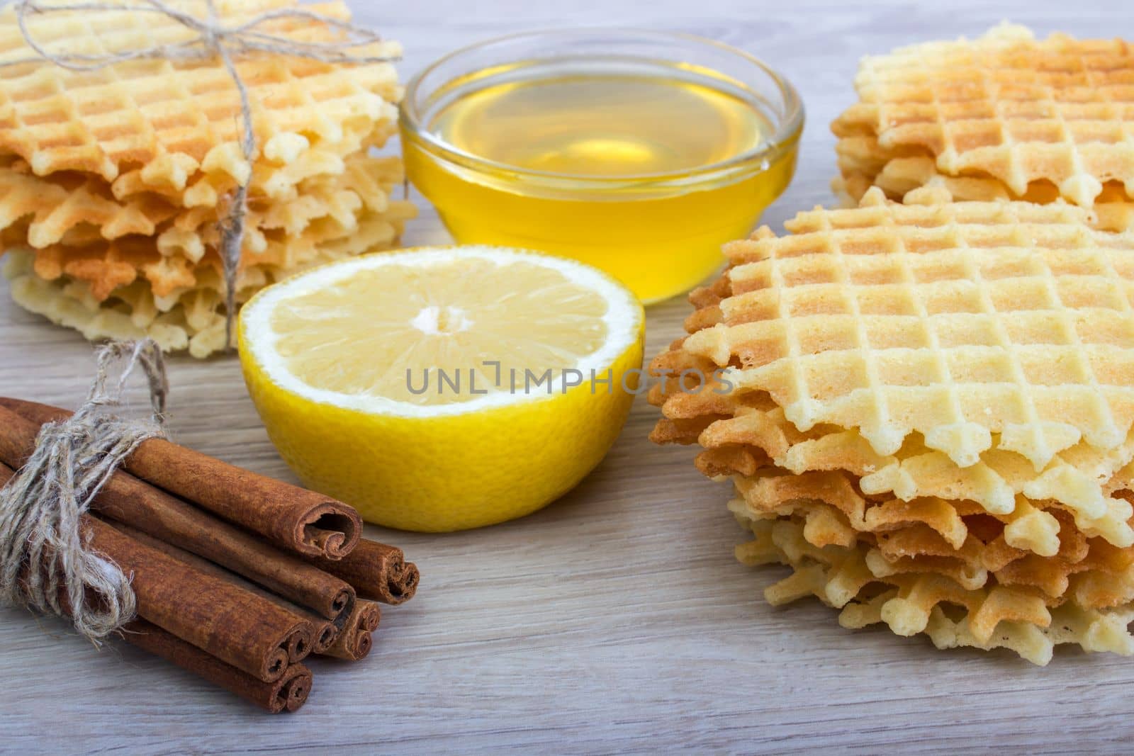 Waffle with honey,cinnamon, lemon on a light wooden background.