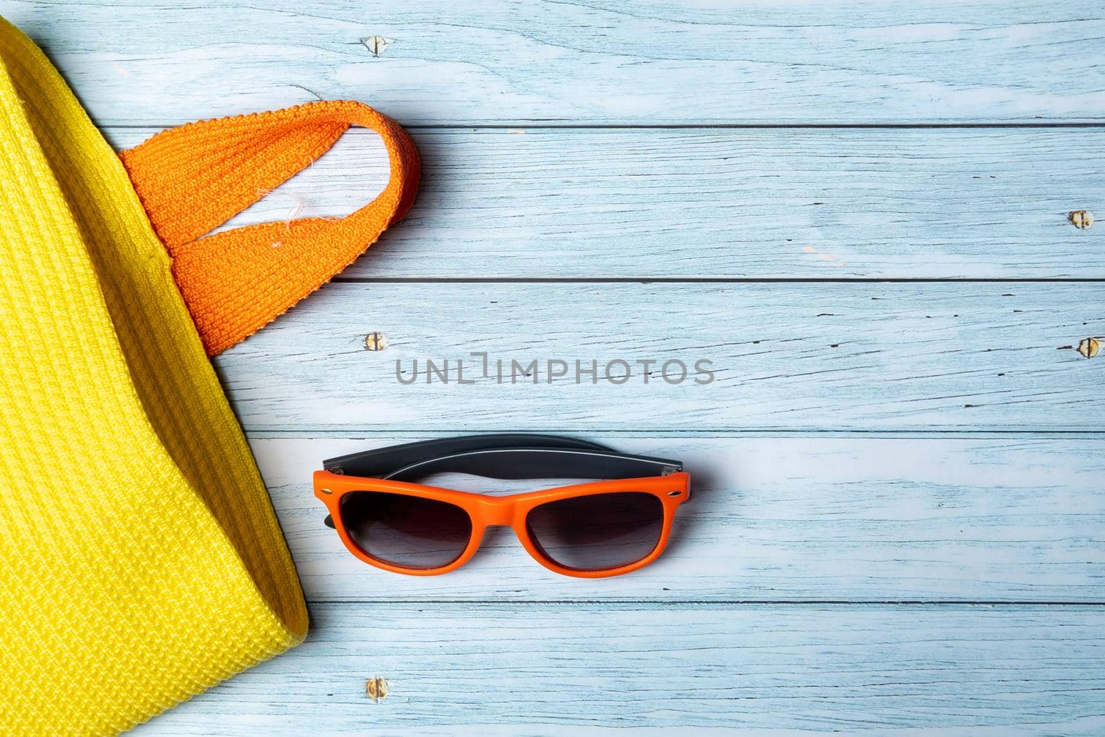 An empty bag with a handle and sunglasses lying on a blue wooden background.