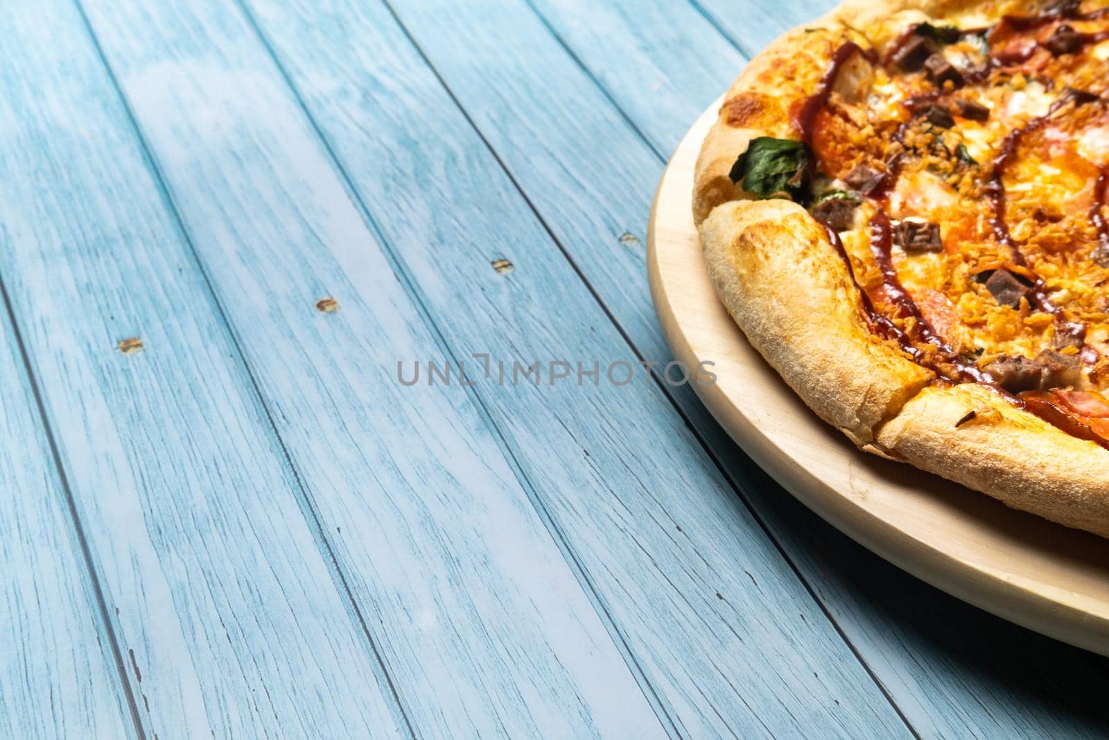 Delicious large pizza with bacon and spinach on a blue wooden background.