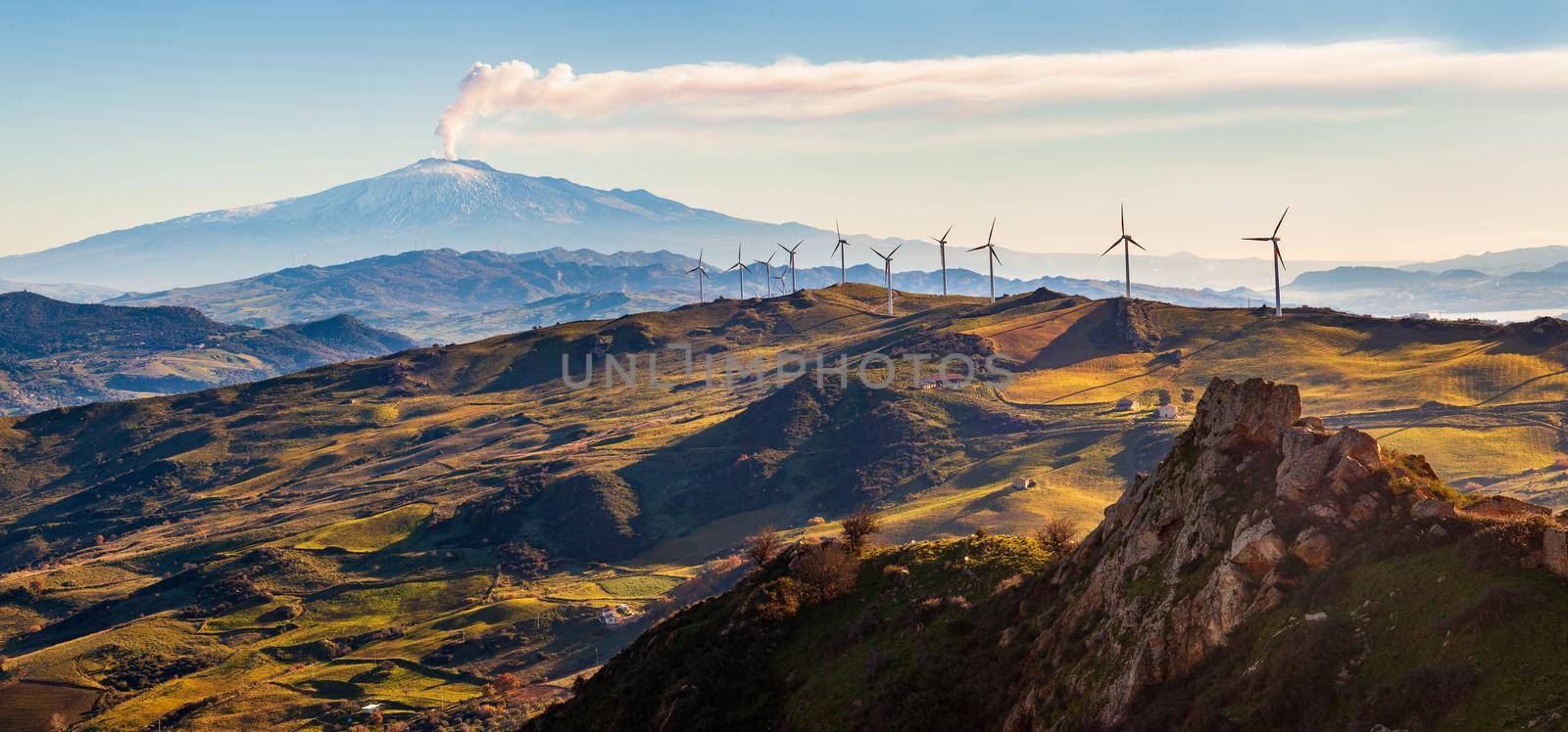 View of windmills and the mount Etna Volcano with smoke. Sicily