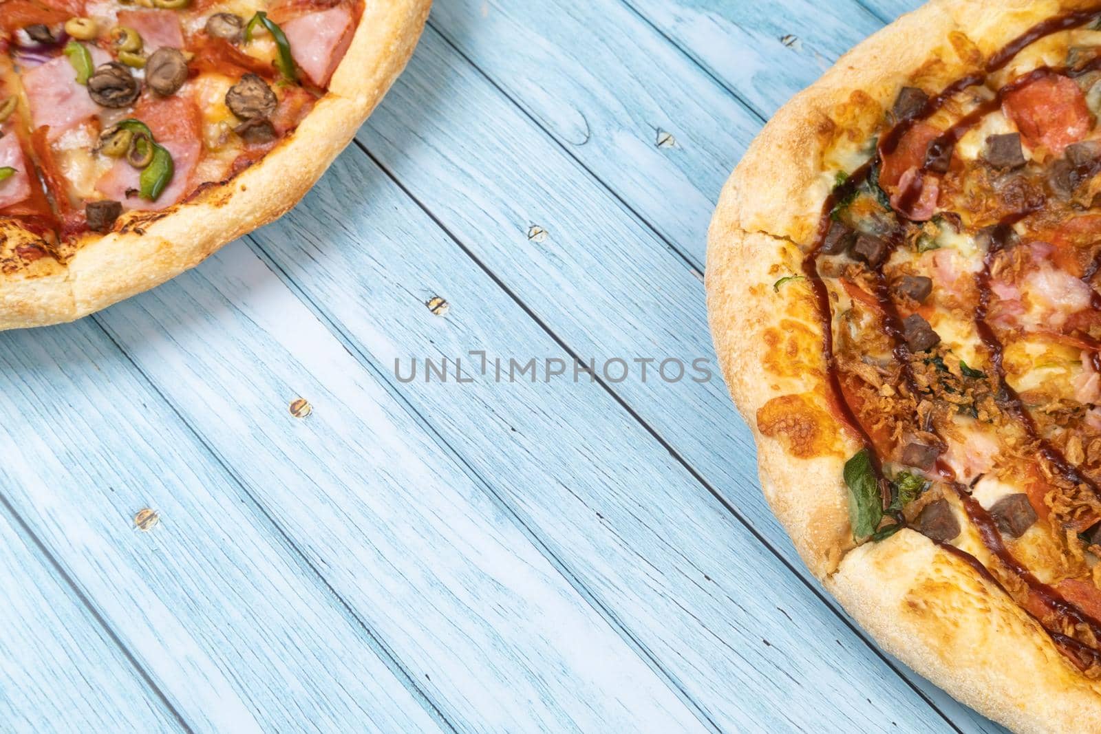 Two different delicious big pizzas on a blue wooden background by Lobachad