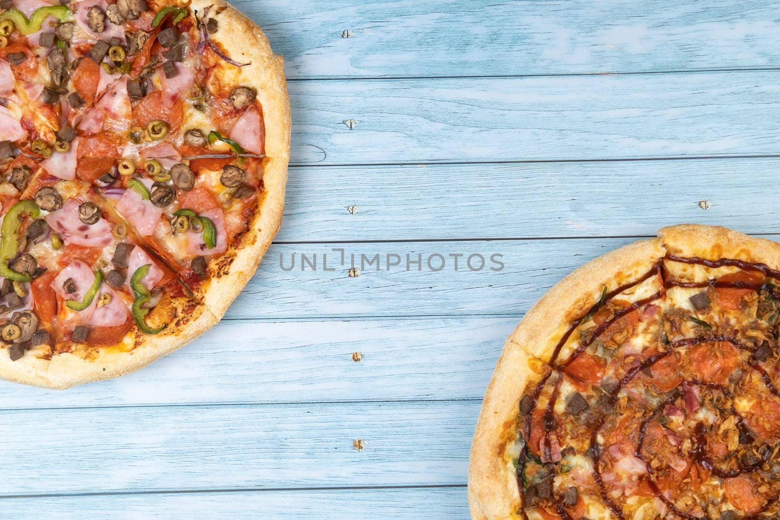 Two different delicious big pizzas on a blue wooden background.