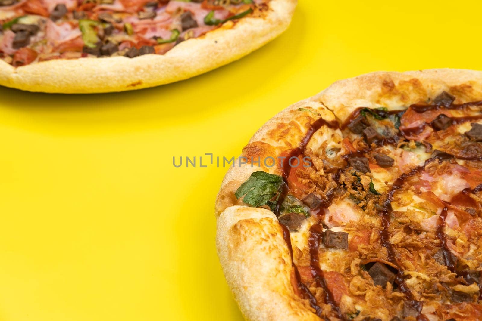 Two different Delicious big pizzas on a yellow background.