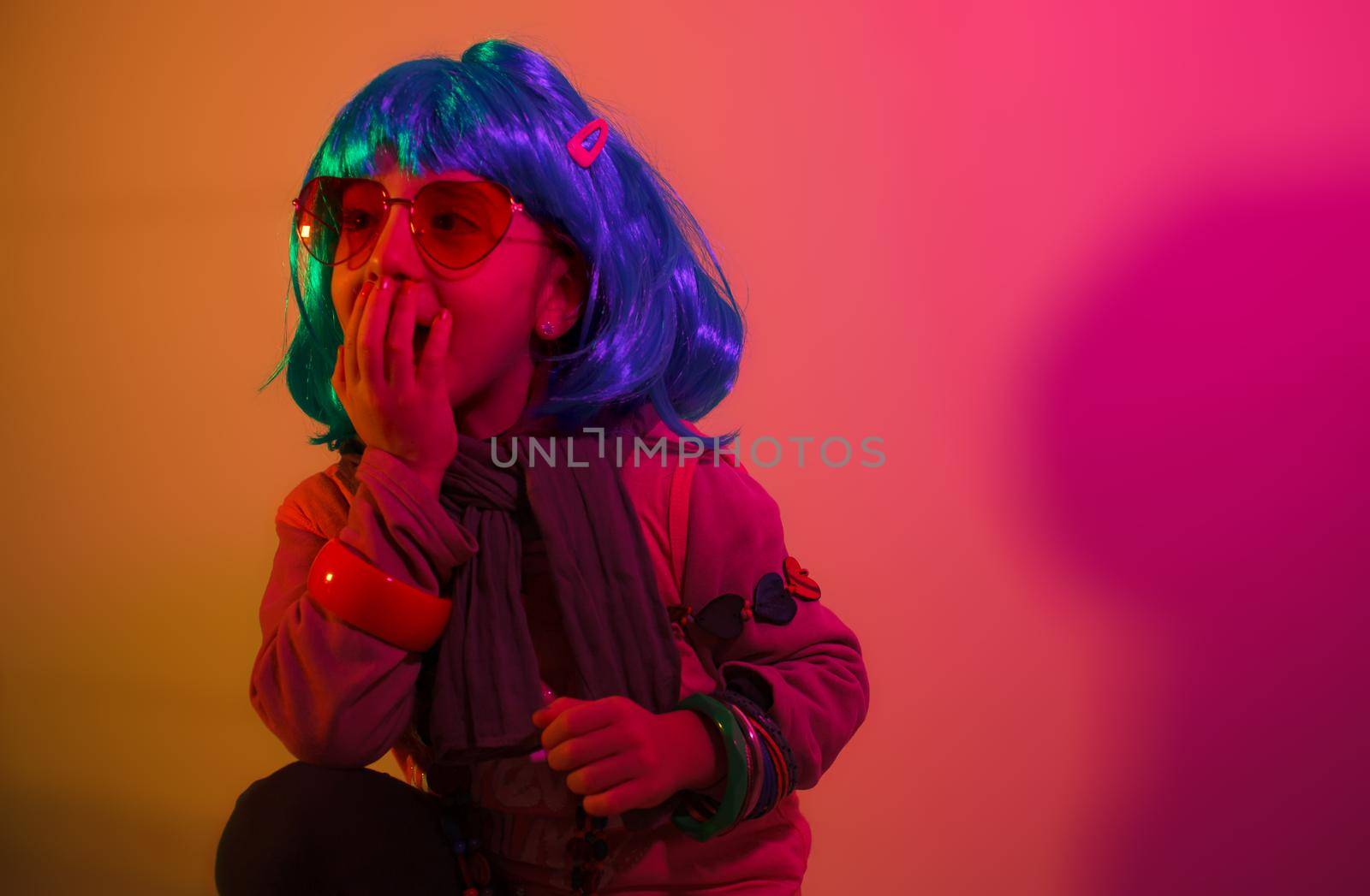 A glamour little girl posing for a photo portrait while wearing a colorful wig on orange background