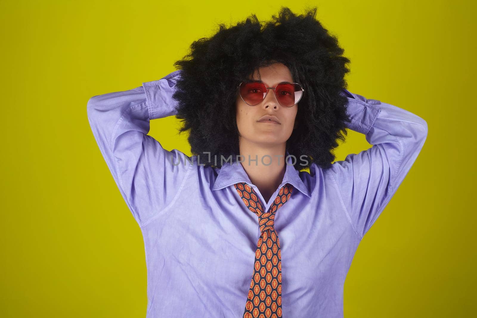 Beautiful woman with afro curly hairstyle wearing sunglasses, male shirt and necktie on yellow background by bepsimage