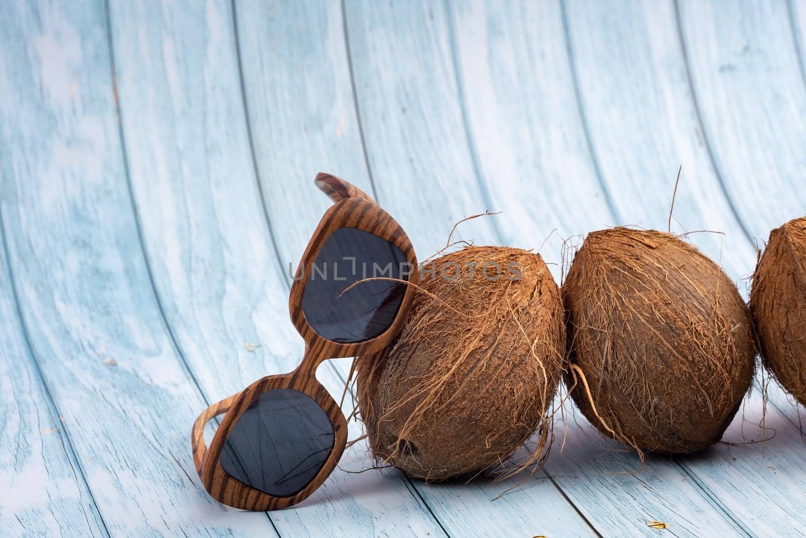 three whole coconuts and wooden glasses on a blue wooden background by Lobachad