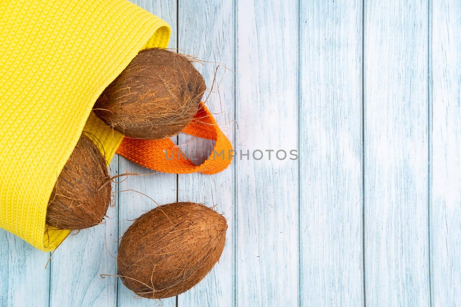 Whole coconuts lying in a yellow bag on a blue wooden background.