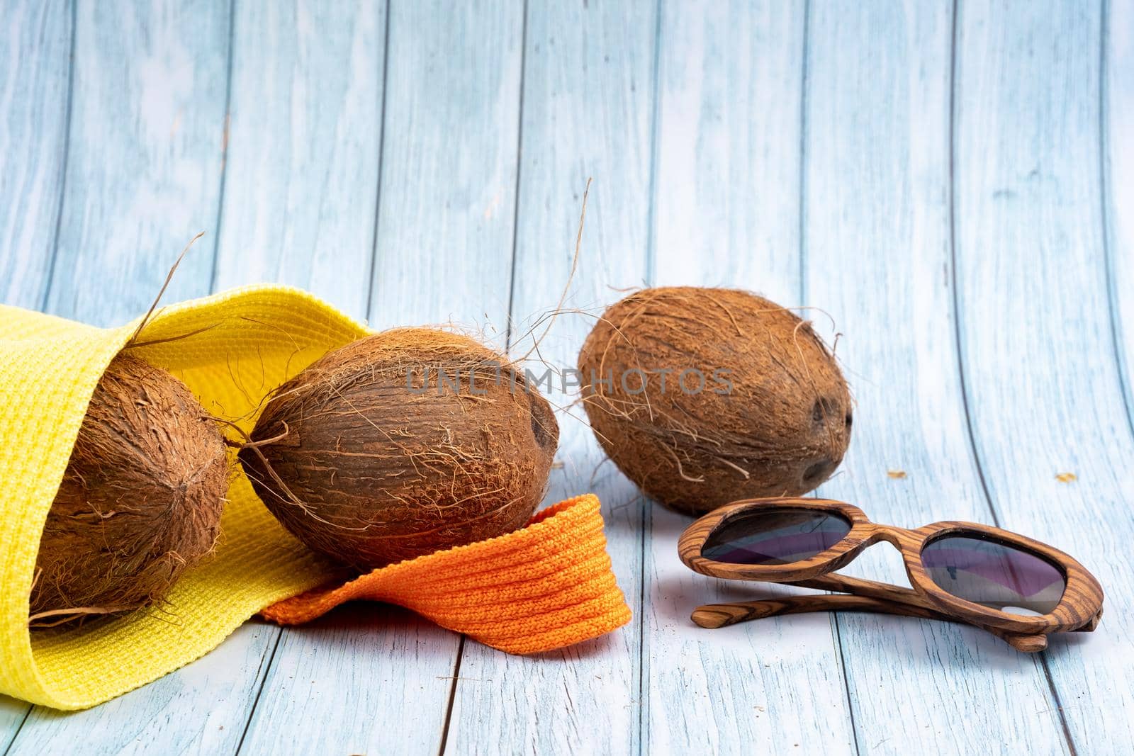 Whole coconuts lying in a yellow bag and glasses on a blue wooden background.