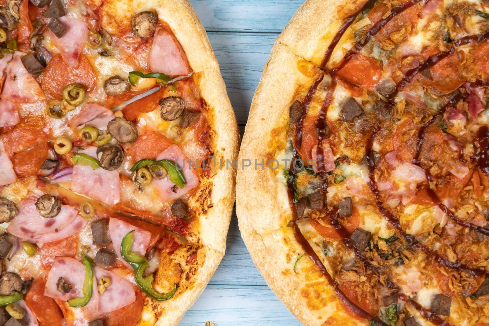 Two different delicious big pizzas on a blue wooden background.