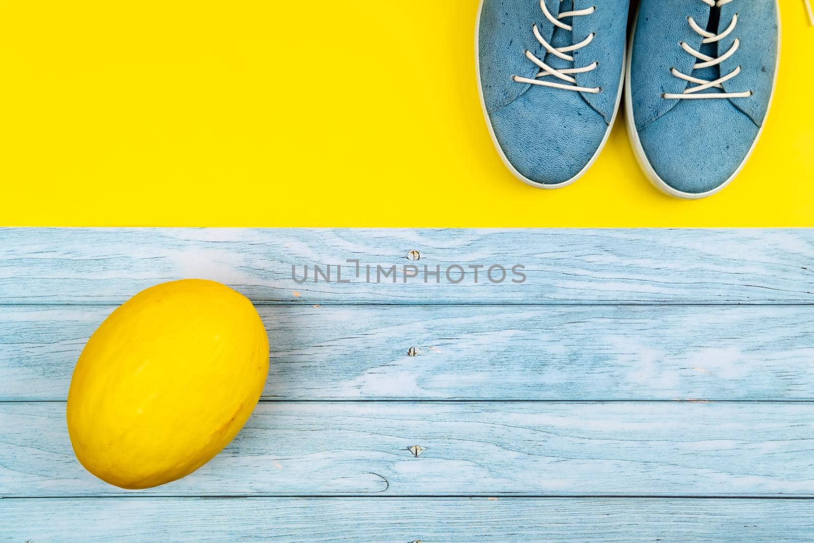 Blue shoes and a melon stand on an isolated mixed blue and yellow background by Lobachad