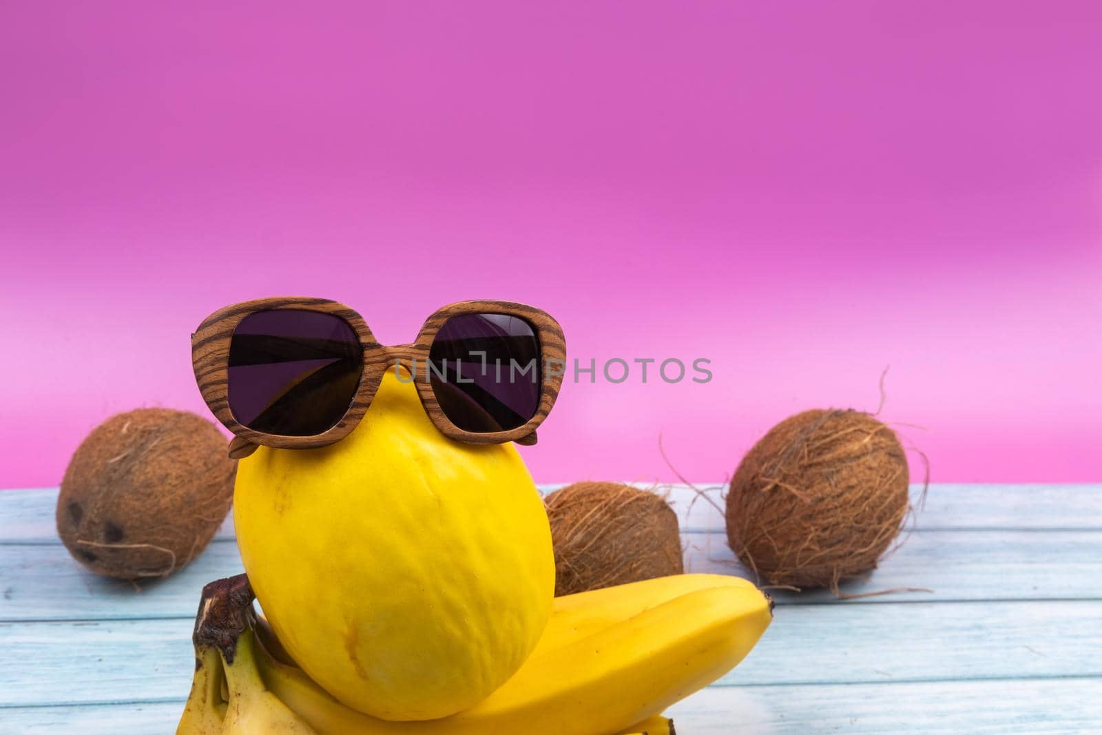An assortment of yellow fruits and glasses lies on a pink background.
