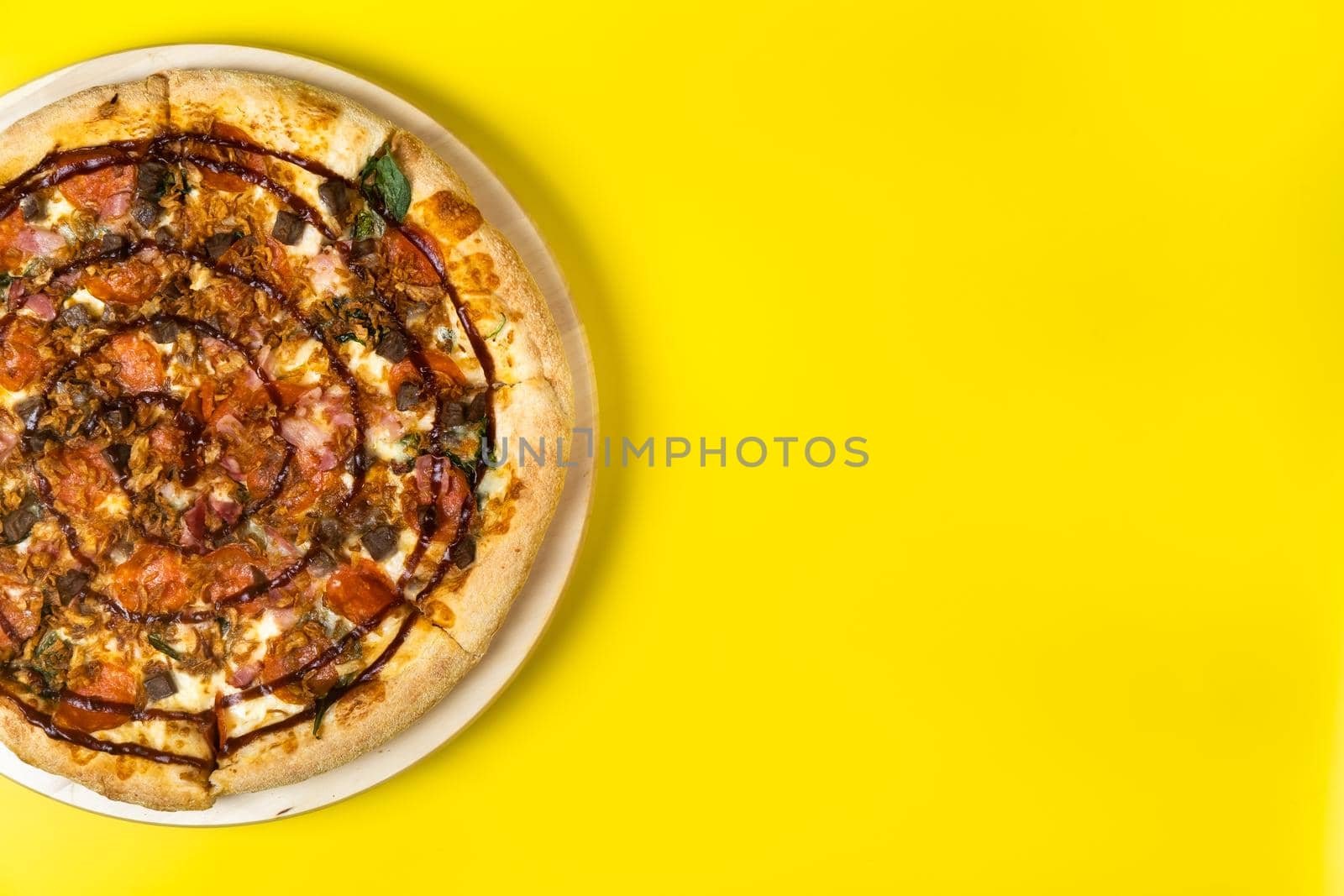 Delicious large pizza with bacon and spinach on a yellow background.