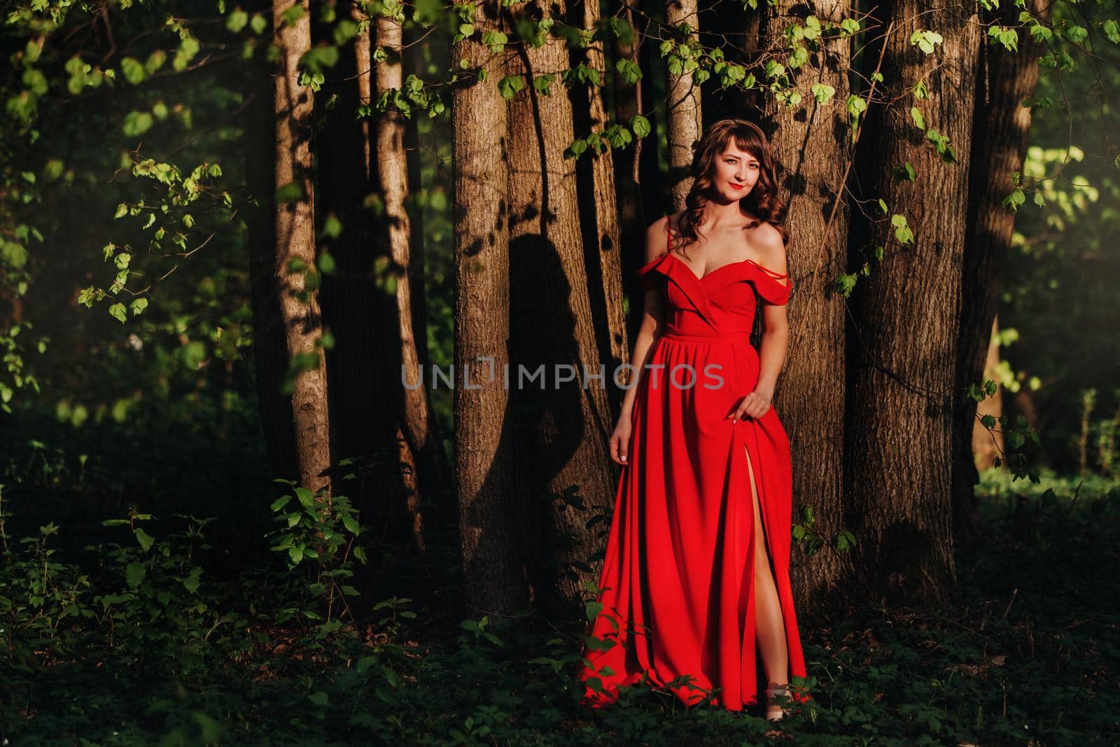 Spring Portrait of a laughing girl in a long red dress with long hair walking in the Park in the woods