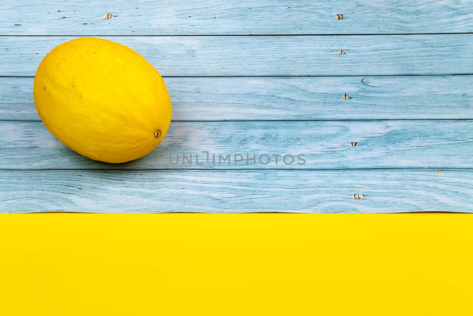 A whole yellow melon lies on a blue wooden background and a yellow background.
