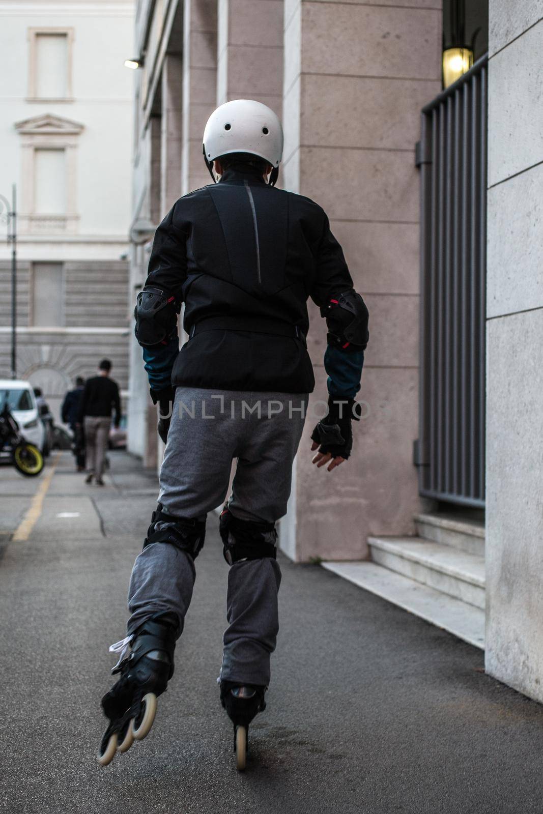 A man wearing helmet and knee pads on roller skates riding outdoors on urban street by bepsimage