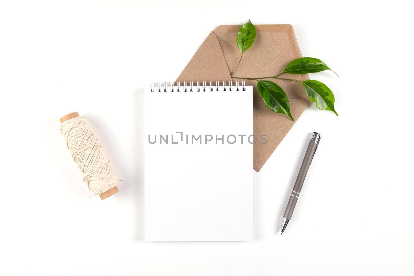 Notebook, recycled paper envelope and spool of plain coarse thread lie on white surface with sprig of green plant. Ecology concept, recyclable, no waste, office, business. Selective focus. Copy space.