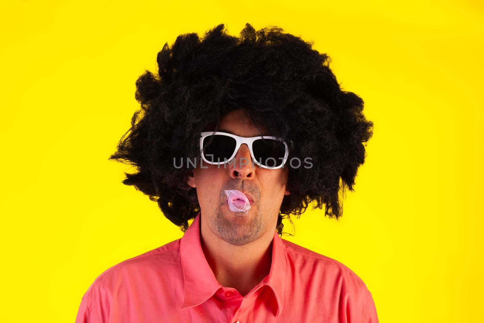 Curly man wearing sunglasses blowing bubble with chewing gum by bepsimage