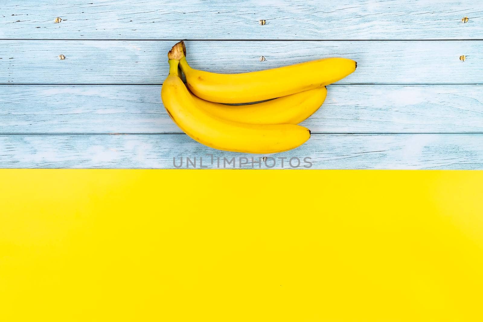 Yellow bananas lie on a blue wooden background and a yellow background.