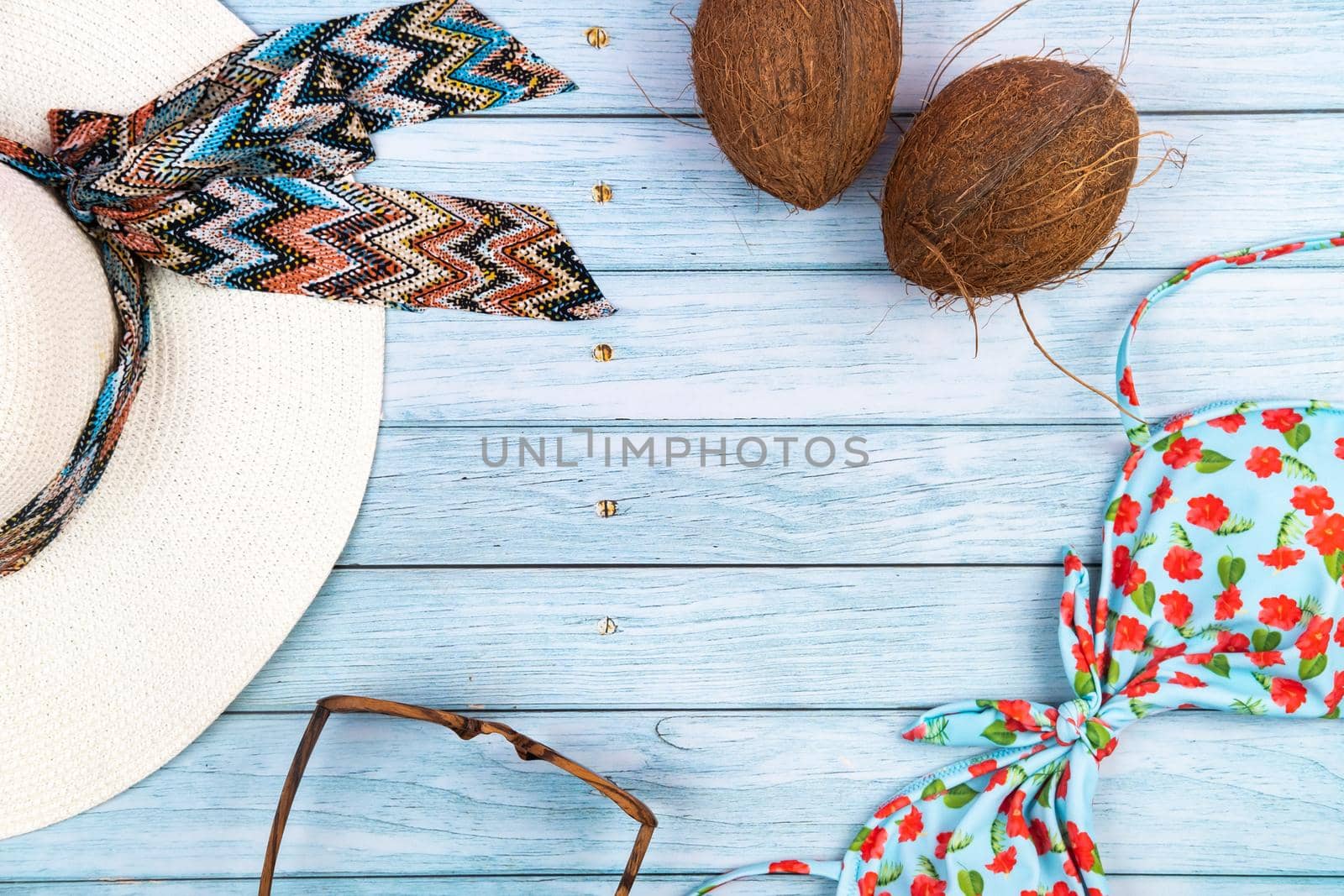 Top view of a straw white hat with glasses, a swimsuit and a coconut lying on a blue wooden background.Summer vacation concept.