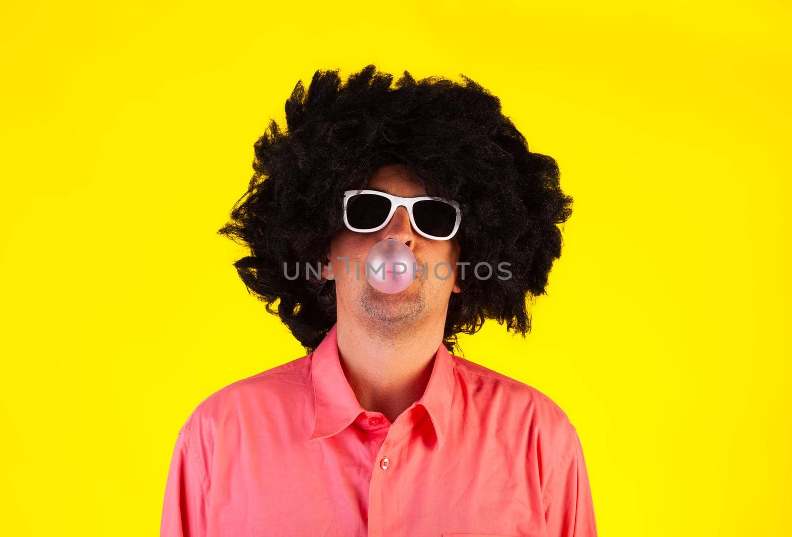 Curly man wearing sunglasses blowing bubble with chewing gum by bepsimage