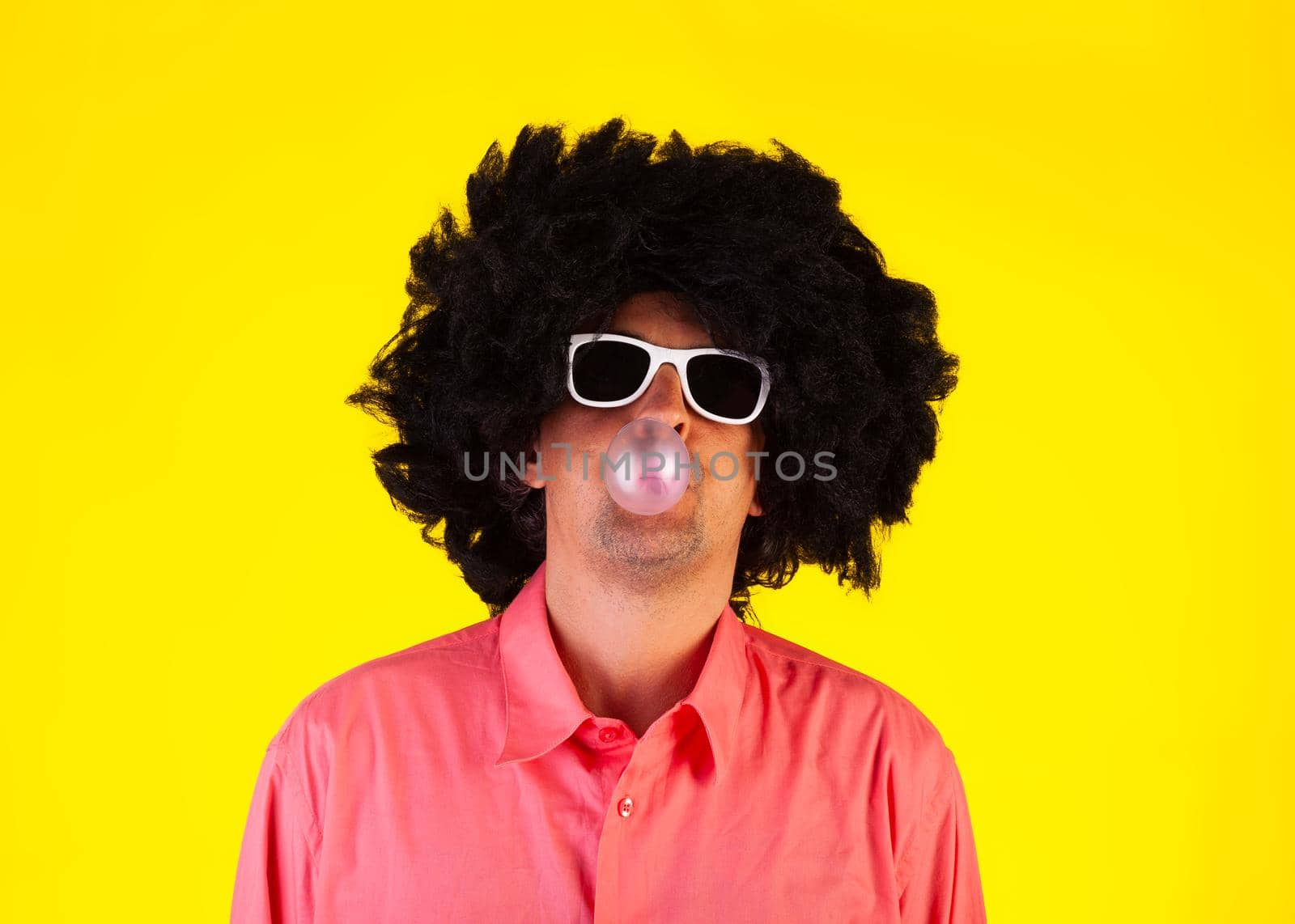 Curly man wearing sunglasses blowing bubble with chewing gum by bepsimage