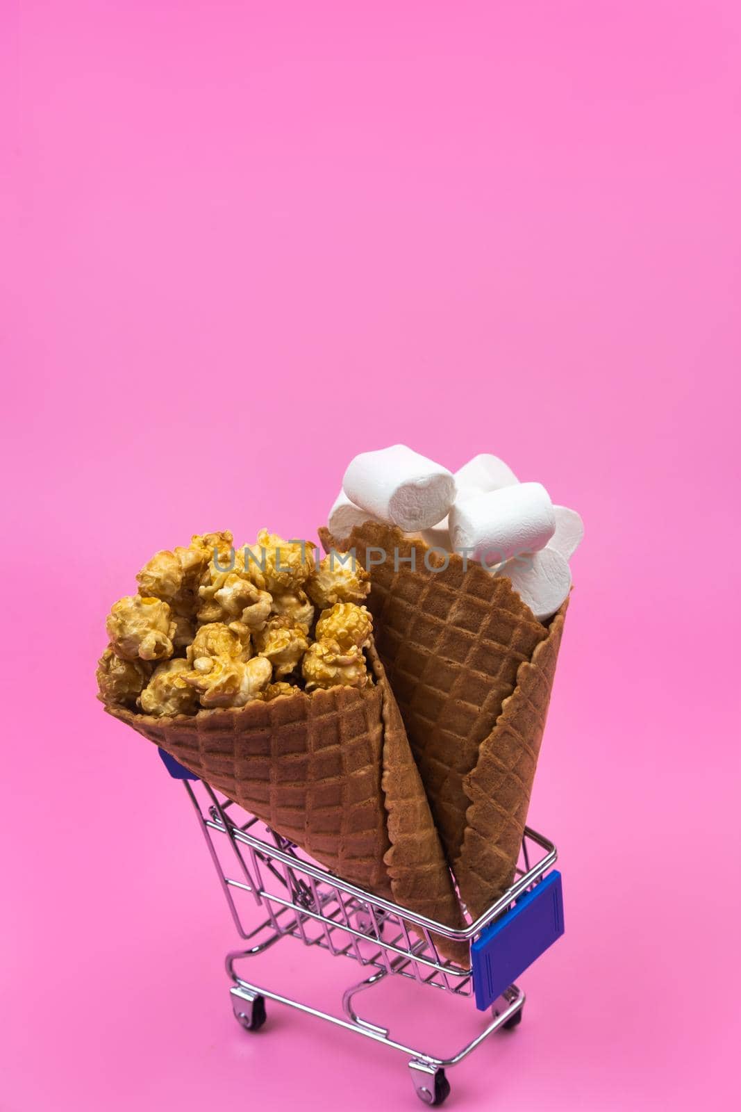 Shopping cart with ice cream cones with sweets on a pink background.