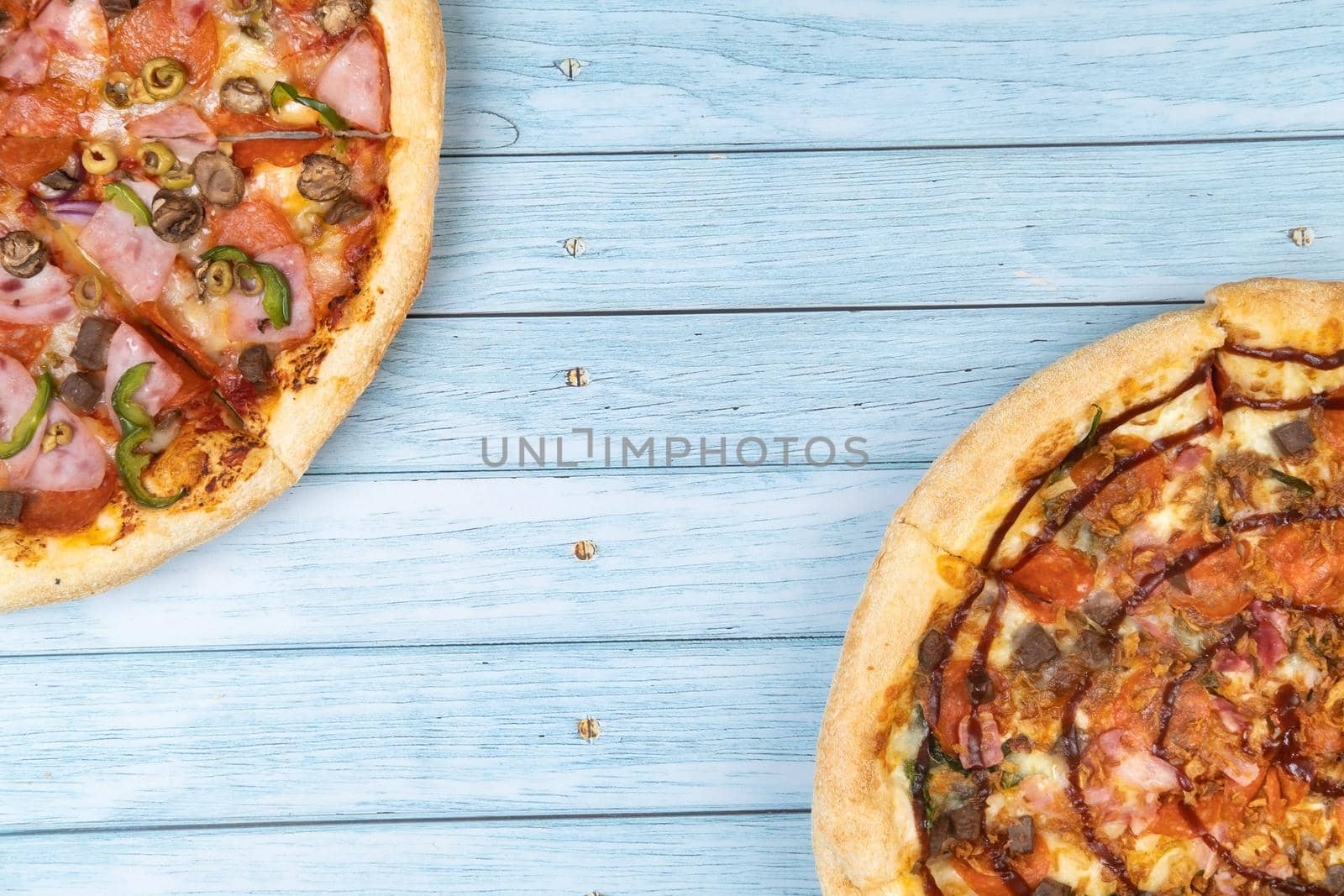 Two different delicious big pizzas on a blue wooden background by Lobachad