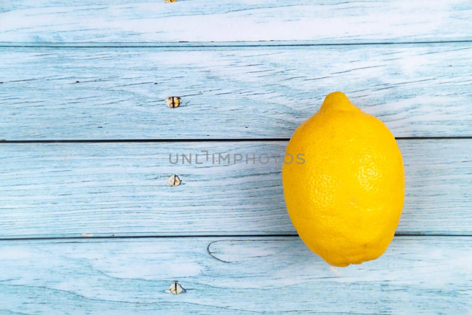 A whole yellow lemon lies on a blue wooden background by Lobachad