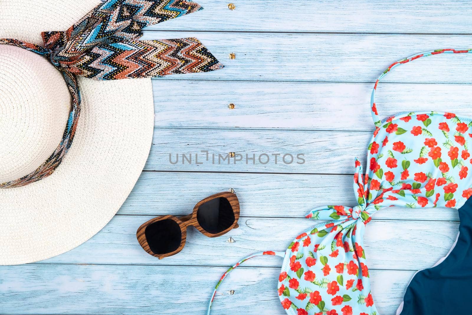 Top view of a straw white hat with glasses and a swimsuit, lying on a blue wooden background.Summer vacation concept.