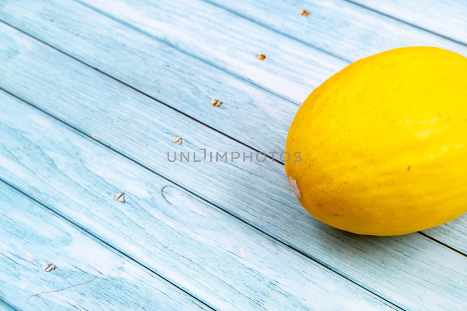 A whole yellow melon lies on a blue wooden background.Summer concept by Lobachad