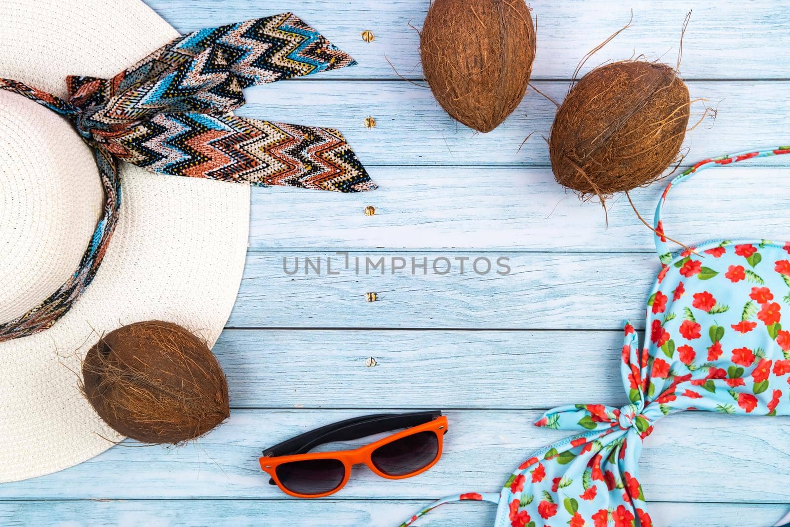 Top view of a straw white hat with glasses, a swimsuit and a coconut lying on a blue wooden background.Summer vacation concept.