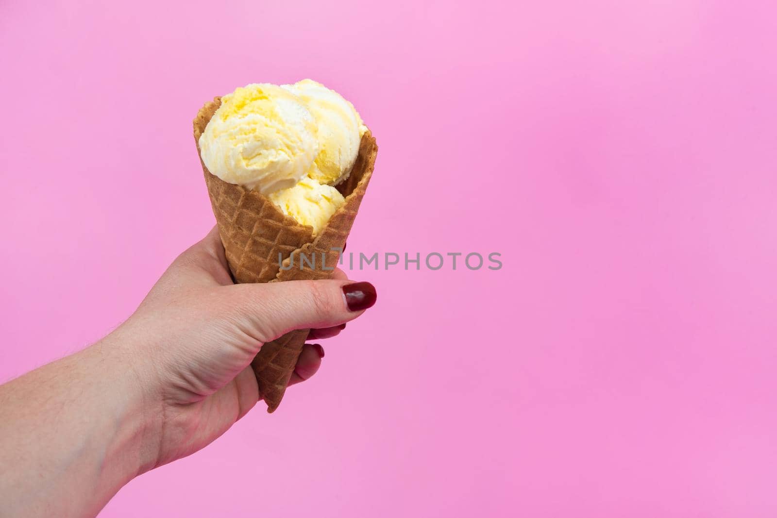 A hand holds an ice cream cone on a pink popsicle background in a waffle cup