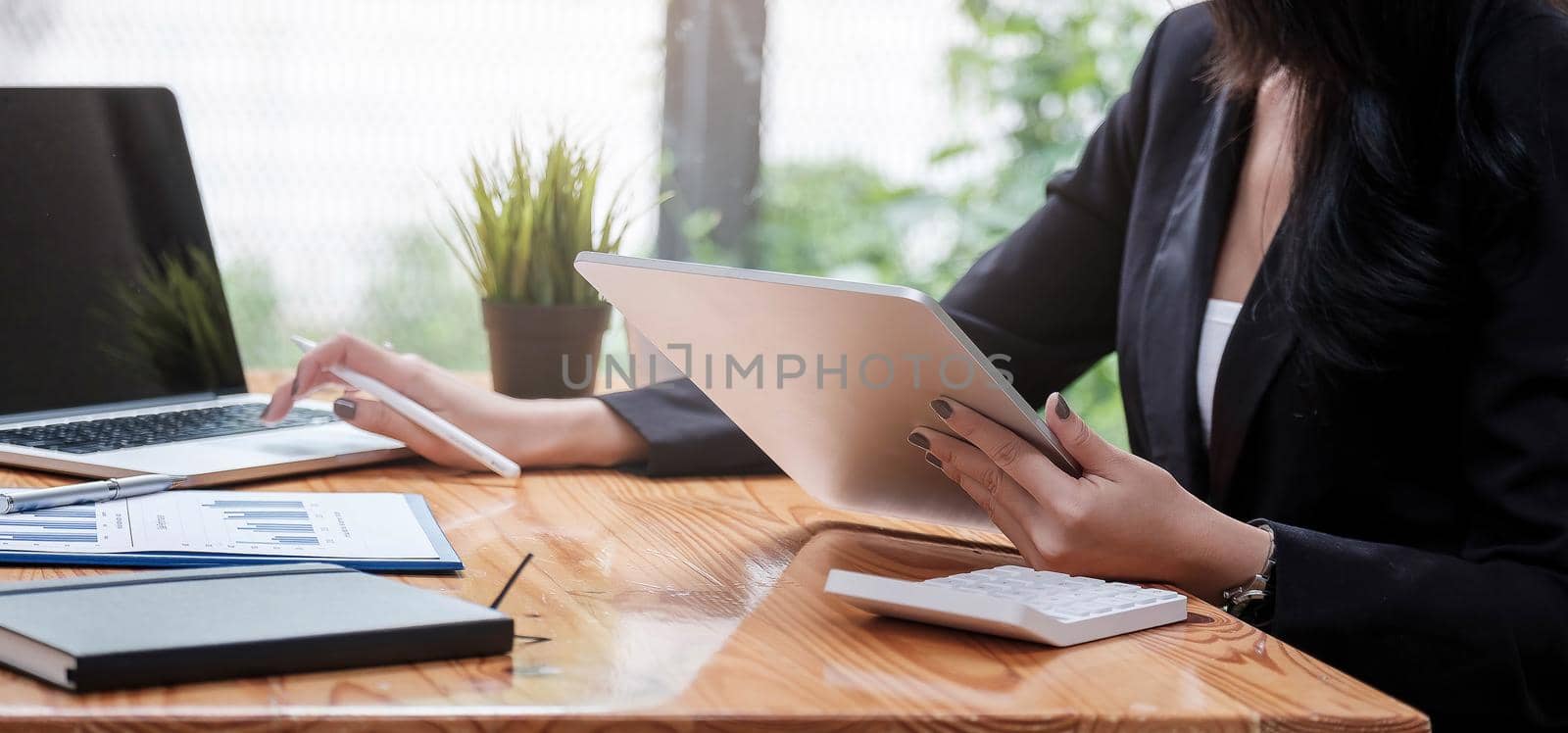 Business woman or accountant hand using calculator, working on taplet and laptop computer with documentary data graph paper on the table at modern home office. Online marketing concept..